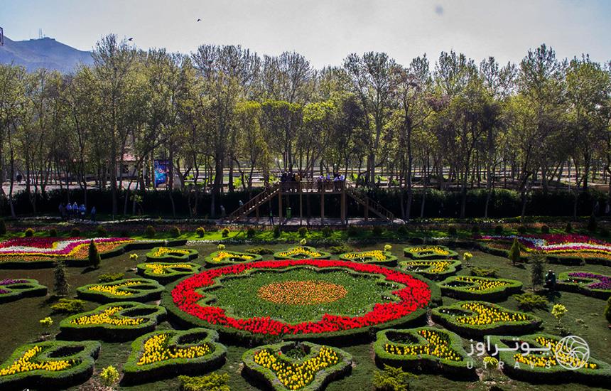 فرشی از گل به رنگ‌های سبز، زرد و قرمز در باغ لاله‌های کرج که سکویی چوبی در کنار آن قرار دارد و چند نفر روی آن ایستاده‌اند